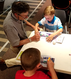 A grandfather helps his grandsons with a circuits activity at the Library Station's Maker Camp.